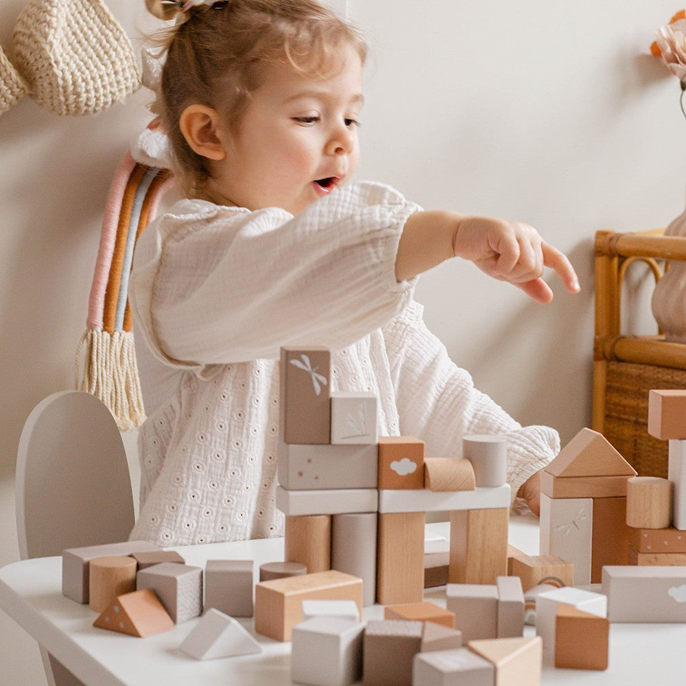 Ein kleines Mädchen spielt mit den Holzbausteinen in der Farbe beige.