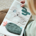 Ein Aktivitätenbuch wird von Kinderhänden geöffnet und es wird gelesen. Die Seite zeigt das Lama und zwei Kakteen.