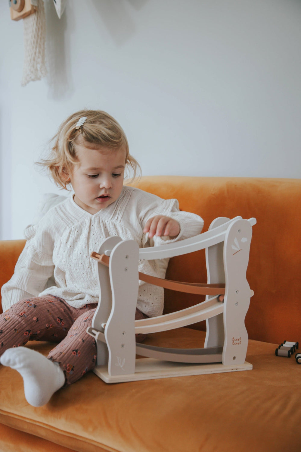 Ein kleines Mädchen spielt mit der beigen Autorutsche auf der Couch.